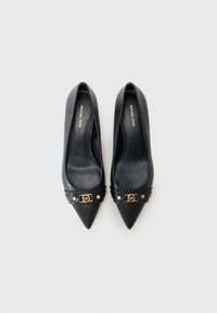 Décolleté neri in pelle con punta appuntita, caratterizzati da un logo in oro e dettagli in borchie sulla cinghia. Finitura liscia e design elegante.