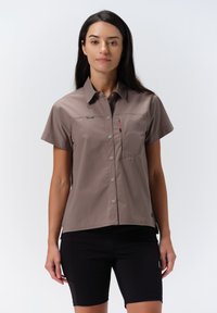 Korte mouwen, overdracht blouse in lichtbruin stof, met een borstzak en subtiele merkdetail op de linkerkant van de borst.