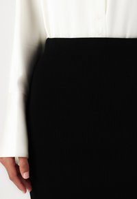 Fustă neagră din tricot cu nervuri, cu talie înaltă, asociată cu o bluză albă cu mânecă lungă, având detalii cu nasturi pe față.