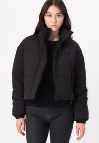 Crna skraćena puffer jakna s quilted dizajnom, koja ima visoki ovratnik, prednji zatvarač i rebraste manžetne. Jednostavna, bez dodatnih uzoraka ili akcenta.
