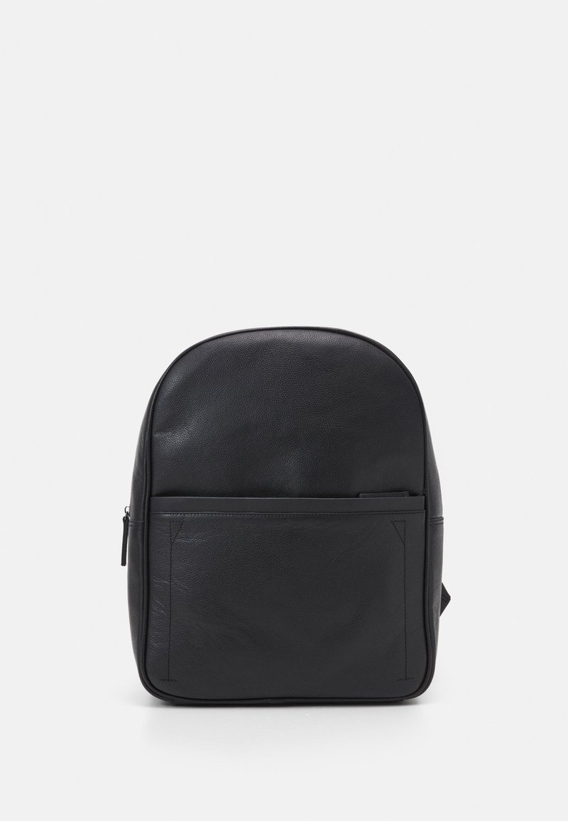 Sac à dos en cuir noir avec une poche avant zippée sur un fond gris clair uni.