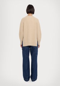 Suéter beige de canalé con aberturas laterales, combinado con pantalones cargo de mezclilla oscura de pierna ancha que cuentan con múltiples bolsillos y detalles de costura.