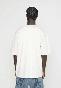 Bílé oversized tričko s krátkými rukávy, vyrobené z měkké látky. Oblečené s modrými džíny z denimu, které mají dekorativní švy na kapsách.