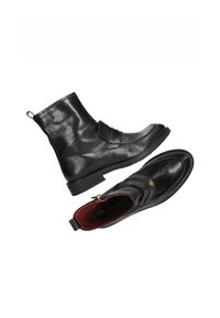 Botas negras de piel hasta el tobillo con una textura suave, correa decorativa, herrajes de acento dorado y un forro interior rojo en contraste.