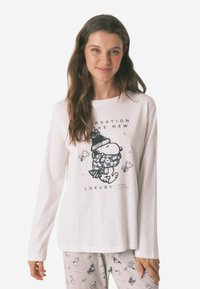 Wit, katoenen t-shirt met lange mouwen met een print van een cartoonfiguur met een hoed en sjaal. De tekst luidt "ONTSPANNING DE NIEUWE LUXE."