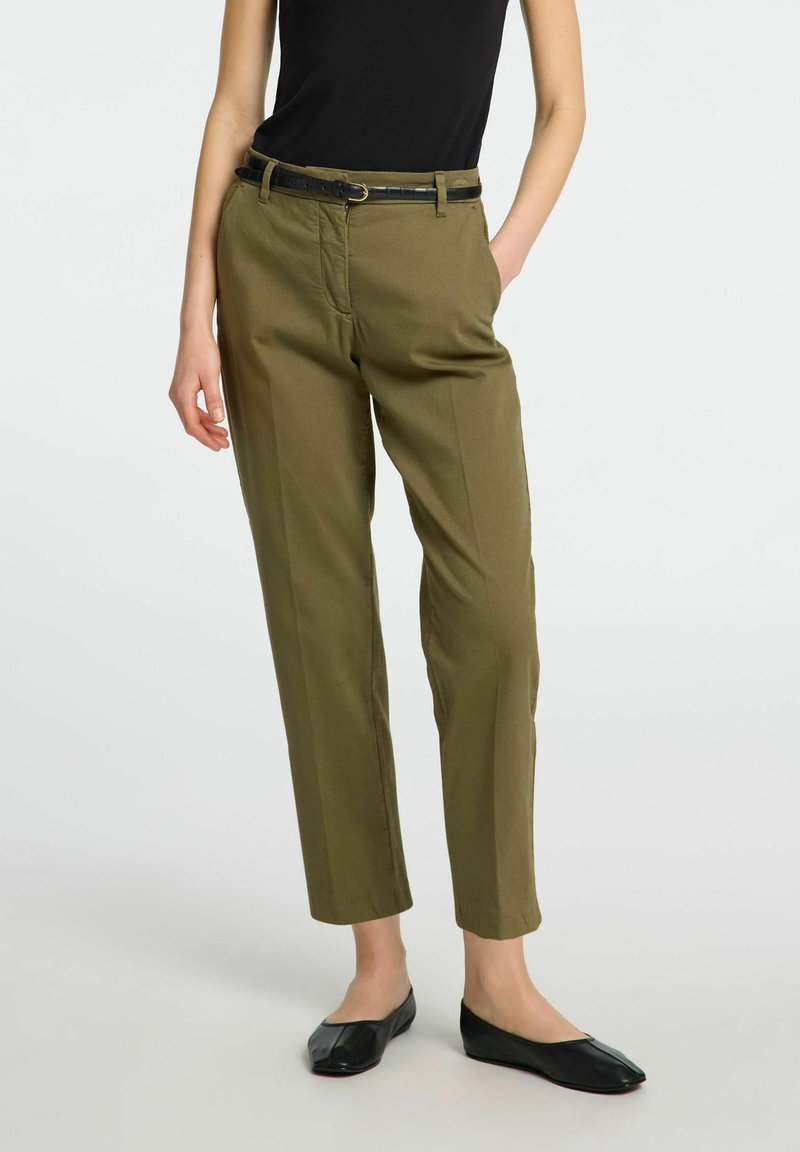 Olivgrüne Hosen mit geradem Schnitt, ausgestattet mit einem schwarzen Gürtel. Glattes Material mit Seitentaschen und einem schlichten Design. Schwarze flache Schuhe.