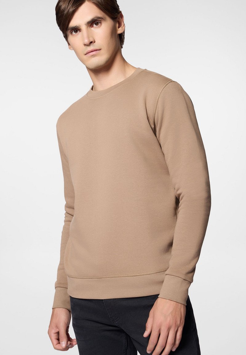 Brązowy sweter z okrągłym dekoltem, z długimi rękawami, ściągaczami przy rękawach i na dole; wykonany z miękkiego materiału, o gładkiej fakturze i minimalistycznym designie.