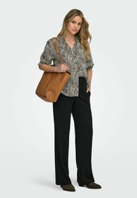 Camisa de botones con estampado de animal en blanco y negro, pantalones de pierna ancha negros y un bolso de cuero marrón claro. El modelo lleva zapatos oscuros con puntera puntiaguda.