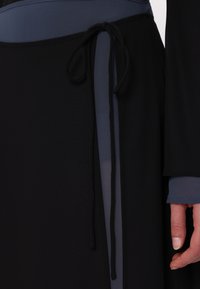 Czarna odzież z teksturowaną górną częścią i gładką, zwiewną dolną częścią, z szarym akcentem i wiązanym detalem w talii.