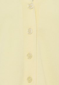 Tissu tricoté jaune doux avec quatre boutons ronds translucides fixés au centre, montrant les boutonnières et les détails de couture.