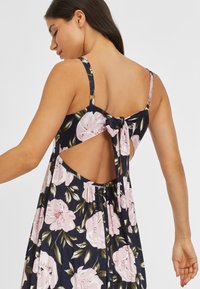 Kleid mit Blumendruck in Marineblau, mit rosa Blumen und grünen Blättern, mit Bindeband auf der Rückseite und offenem Design. Hergestellt aus einem weichen, fließenden Stoff.