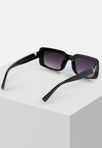 Czarne prostokątne okulary przeciwsłoneczne z gradientowymi ciemnymi soczewkami, odważnym designem oprawki, błyszczącym wykończeniem oraz charakterystycznymi metalowymi akcentami na zausznikach.