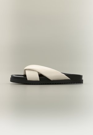 Mustade talladega sandaal laia, risti asetatud valkjate nahkribadega ja tekstuurse tallaga, kujutatud küljelt ühtlasel taustal.