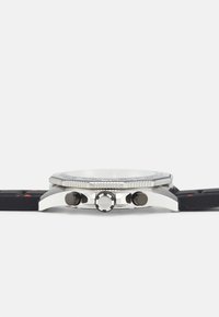 Reloj de acero inoxidable con correa de goma negra, bisel en tono plateado y botones negros. Presenta una esfera redonda con marcadores y acentos claros.