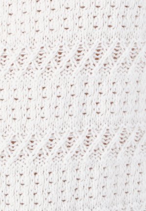 Tela de punto en blanco con un patrón texturizado que presenta líneas diagonales y pequeños puntos marrones, mostrando una artesanía intrincada.