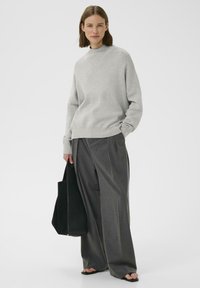 Maglione grigio chiaro lavorato a maglia con un collo alto, abbinato a pantaloni larghi grigio scuro con pieghe e una borsa tote nera. Design semplice e pulito.