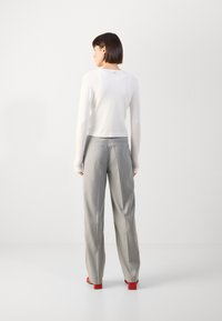 Long-sleeve, white top with a rounded neckline paired with light gray pinstriped trousers and red heeled sandals. Simple, fitted design.