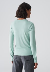 Mintgroene longsleeve shirt met een ronde hals, gladde textuur, slim fit, gecombineerd met donkergrijze jeans, gezien vanachter.