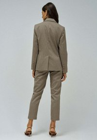 Blazer de cuadros marrones y pantalones a juego. Diseño estructurado con una abertura trasera, corte entallado y detalles de botones en las mangas.
