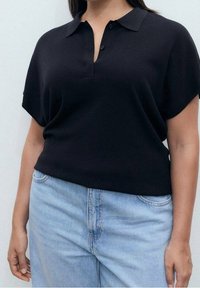 Czarna polo z krótkim rękawem, kołnierzykiem i trzema guzikami, o luźnym kroju. W zestawieniu z jasnoniebieskimi dżinsami.