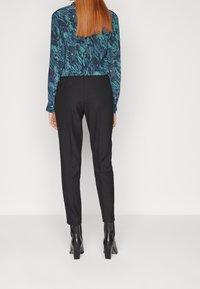 Långärmad blus i mörkblått med turkos marmorering, matchad med svarta smalrandiga byxor och ankelstövlar med klumpig klack.