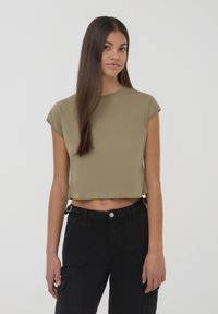 T-shirt cropped verde oliva con maniche corte, realizzato in tessuto morbido. Abbinato a pantaloni cargo neri a vita alta con tasche laterali.
