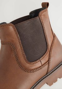 Nahaufnahme eines braunen Leder-Chelsea-Stiefels mit elastischem Seitenbereich und Ziehschlaufe, der die detaillierte Naht und die strukturierte Sohle zeigt.