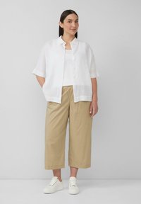 Witte linnen shirt, lichte tanktop en beige wijde broek, gecombineerd met witte sneakers. Het shirt heeft een doorlopende knoopsluiting en korte mouwen.