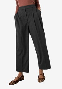 Pantaloni a gamba larga grigio a righe con vita alta e tasche laterali, abbinati a scarpe ballerine con stampa leopardata e dettaglio a fiocco.