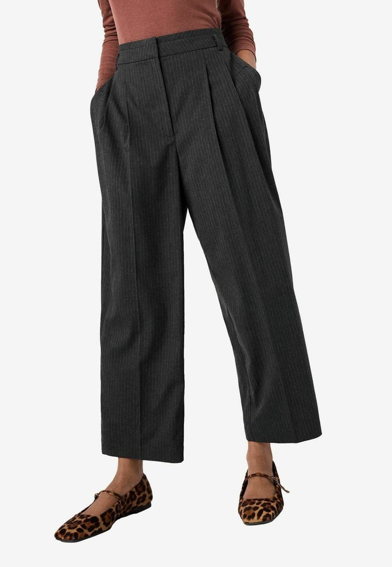 Pantaloni a gamba larga grigio a righe con vita alta e tasche laterali, abbinati a scarpe ballerine con stampa leopardata e dettaglio a fiocco.