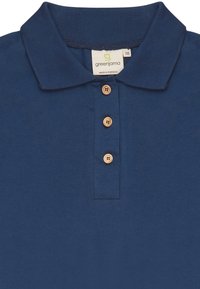 Dunkelblauses Poloshirt aus Baumwolle, mit einem gerippten Kragen, drei Holzknöpfen und einem kleinen Etikett mit der Aufschrift "greenjama" innen am Kragen.
