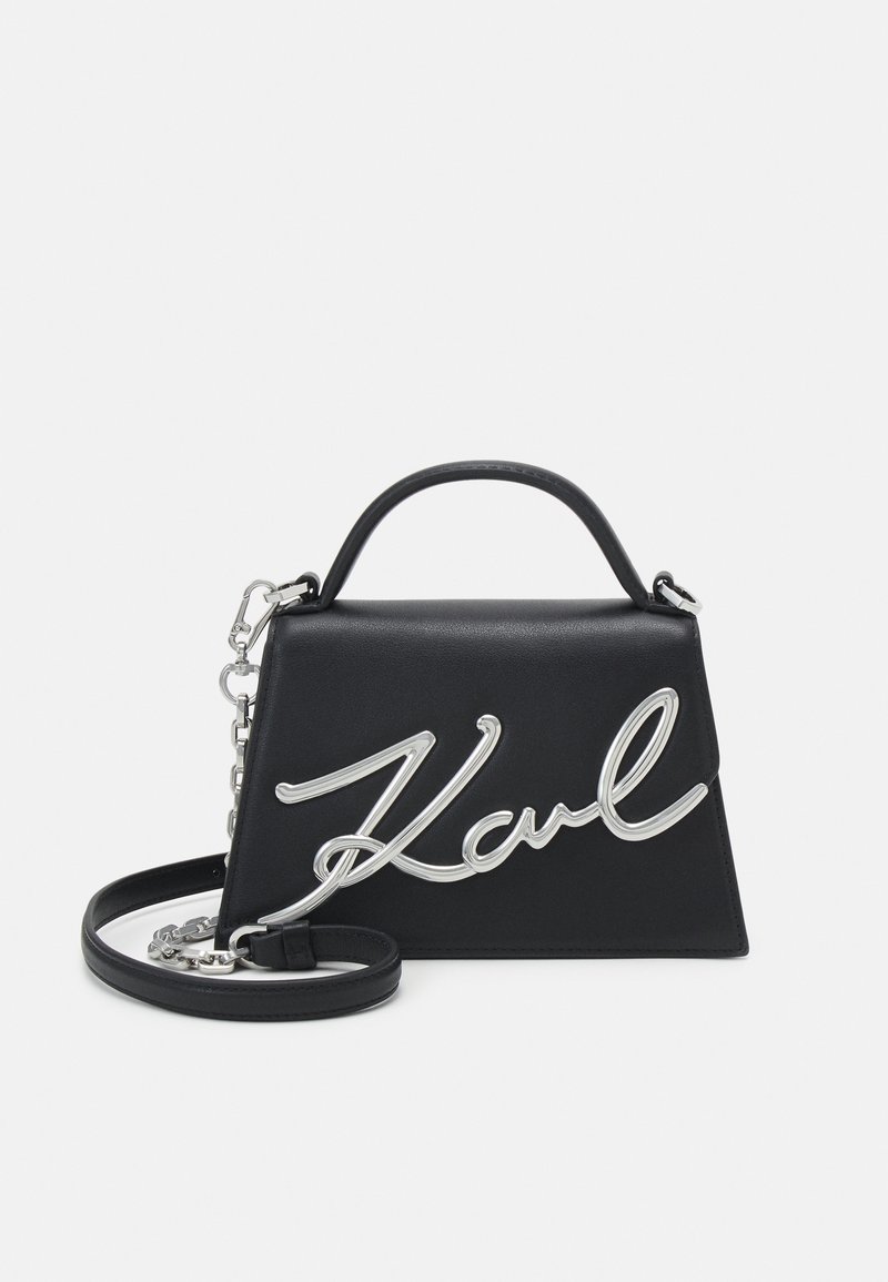 Bolsa de couro preta com formato triangular, destacando-se o logo prateado "Karl", alça superior e alça de ombro destacável.