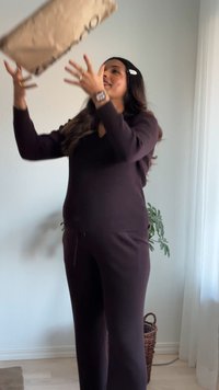 Donna con abbigliamento da salotto scuro che lancia una scatola di cartone all'interno, vicino a una finestra con tende bianche trasparenti e un cesto di vimini.