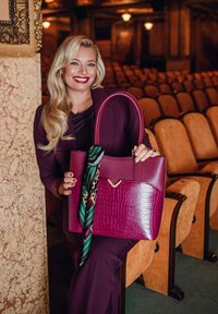 Velká fialová taška přes rameno s krokodýlím vzorem, hladkými akcenty a zeleným vzorovaným šátkem uvázaným na rukojeti.