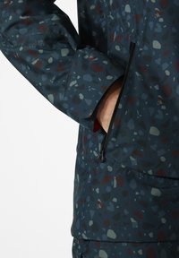 Kurtka typu windbreaker z niebieską bazą i teksturowymi kolorowymi kropkami, z kieszenią zapinaną na zamek oraz zaprojektowanym mankietem.