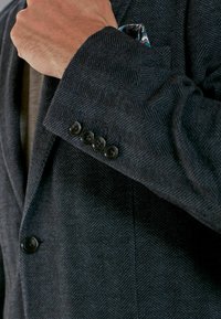 Blazer à motif chevrons sombre avec une fermeture à un bouton, doté de boutons noirs et d'un pochette affichant des motifs floraux.