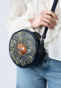 Sac en cuir bleu marine en forme ronde, avec un motif floral brodé et un rongeur dormant. Dispose d'une fermeture éclair dorée et d'une sangle ajustable.