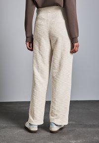 Cremfarbene, strukturierte, weit geschnittene Hose mit hoher Taille, mit Seiten- und Knöchellänge. Kombiniert mit weißen Sneakern.