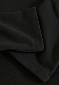 Vêtement noir à manches longues plié pour montrer en gros plan les détails de la texture lisse du tissu et des poignets soigneusement cousus.