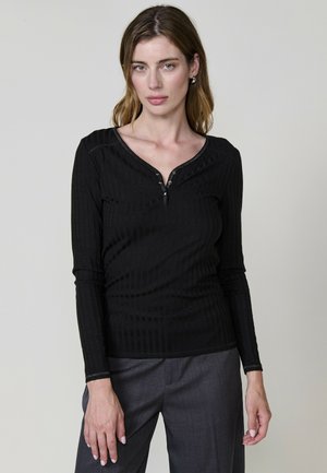 Haut noir à manches longues avec une texture côtelée, présentant un décolleté en V et un plastron à boutons à l'avant, associé à un pantalon gris.