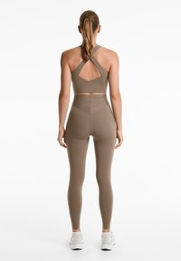 Sporttop en legging in een gedempte bruine tint. De top heeft een unieke uitsnijding op de rug en kruislings bevestigde banden, terwijl de legging een aansluitend ontwerp heeft.