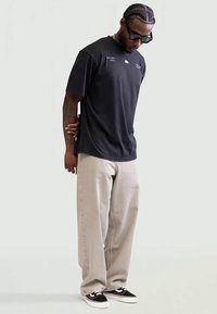T-shirt preta de algodão com detalhes impressos no peito, combinada com calças largas em bege claro e ténis pretos e brancos.