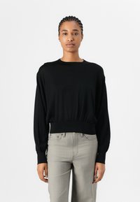 Black long-sleeve top with a round neckline and elasticized hem. Soft fabric; fitted at the waist, loose-fitting sleeves. Paired with light grey pants.