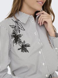 Blusa a righe bianche e nere con colletto e ricamo floreale in perline sul lato sinistro. Bottoni lungo la parte frontale.