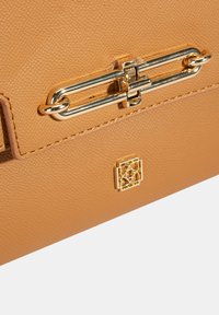 Handtasche aus genarbtem, beige-braunem Leder mit einem goldfarbenen Metallverschluss und einem geprägten Logo auf der Vorderseite. Glatte Oberfläche mit präziser Nahtarbeit.