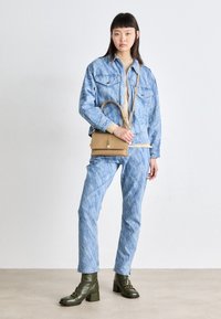 Jasnoniebieska kurtka jeansowa i pasujące do niej dżinsy o fakturowanym wykończeniu, zestawione z ciemnozielonymi botkami za kostkę i małą beżową torebką na ramię.