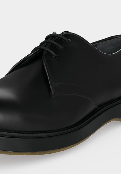 Μαύρο δερμάτινο επίσημο παπούτσι με κορδόνια, λεία επιφάνεια και παχιά λαστιχένια σόλα, φαίνεται από την πλευρά της μπροστινής γωνίας.