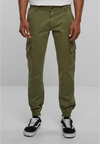 Olijfgroene cargo broek met elastische boorden, voorzien van meerdere zijzakken en een zachte textuur. Gecombineerd met zwarte sneakers en witte veters.