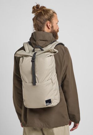 Beige rugzak met een oprolbaar ontwerp, verstelbare banden en een voorzak. Gemaakt van duurzaam fabric met een klein logo-label aan de onderkant.