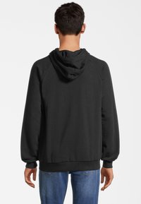 Felpa nera con cappuccio regolabile, maniche a raglan, polsini e orlo a costine. Il tessuto sembra morbido e testurizzato, indossato con jeans blu.